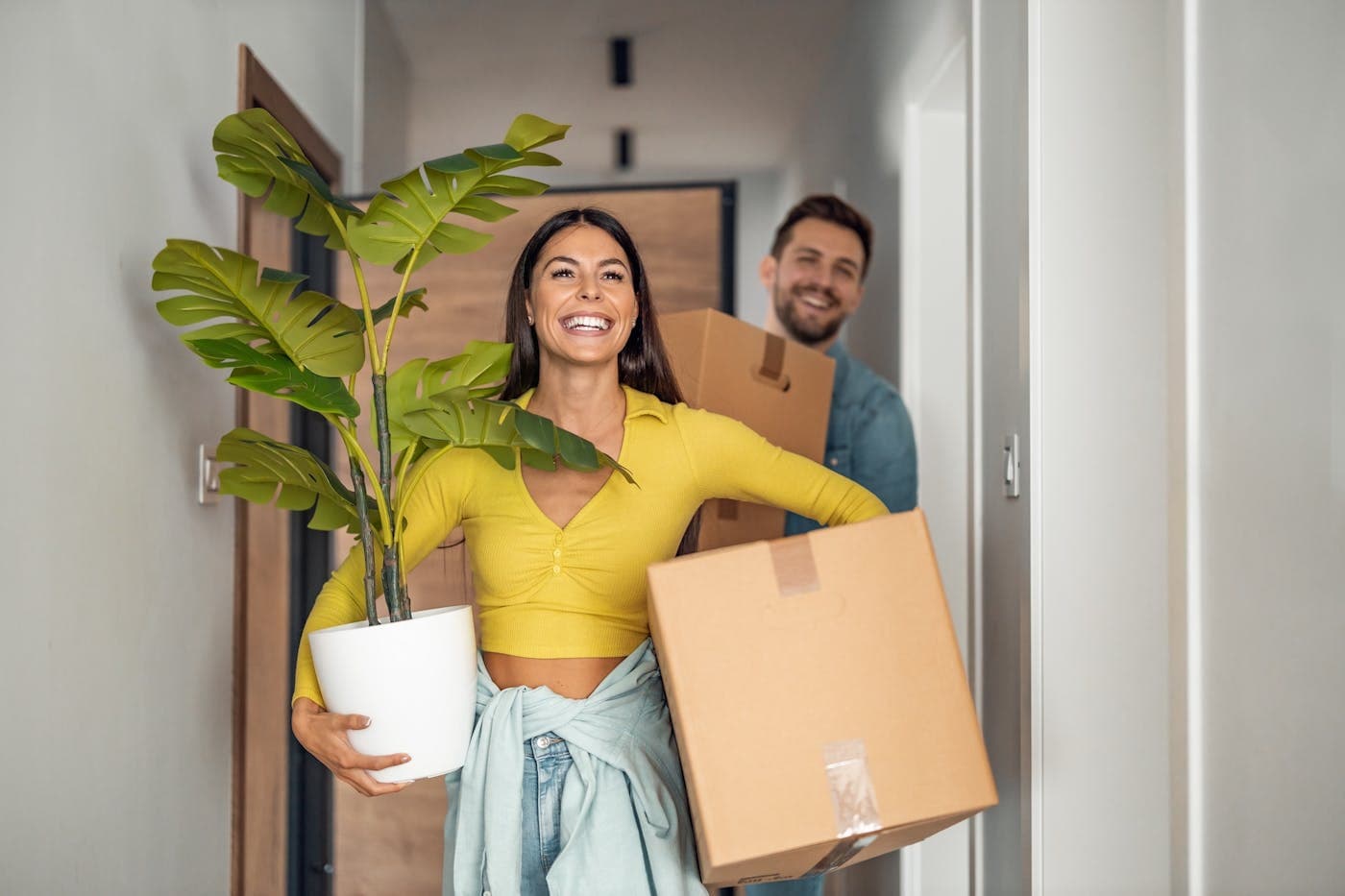 Un couple emménage, une plante et un carton dans les bras.