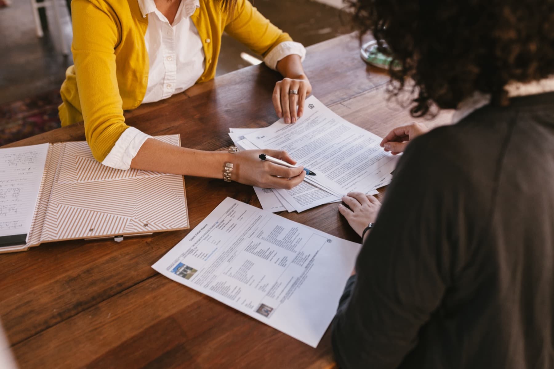 Une main signe un document posé sur une table en bois.